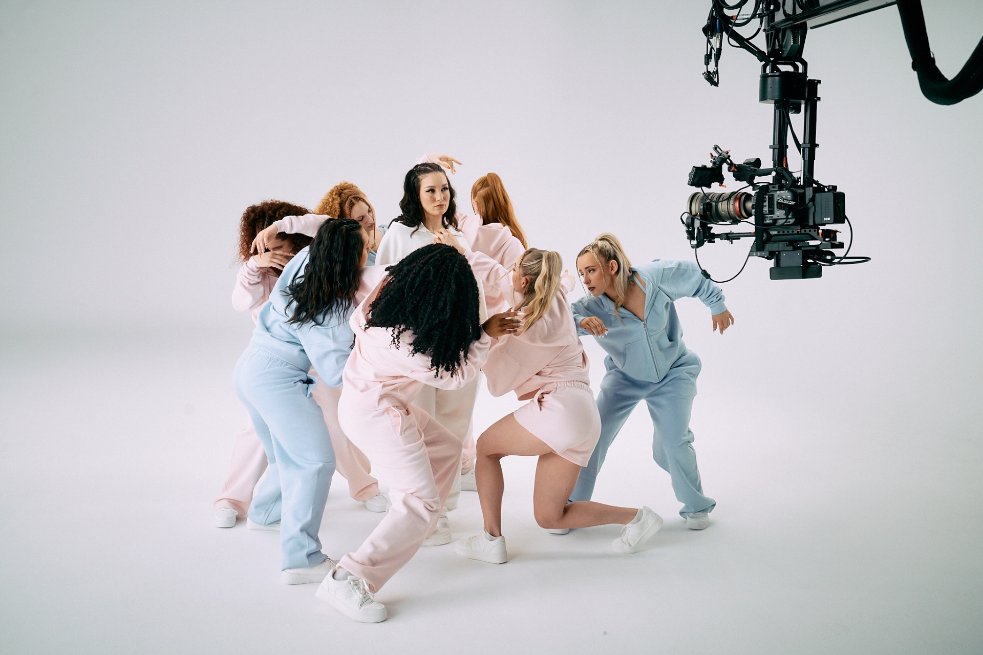 Behind the scenes — cast huddle in pastel pink and blue cfab Spring Collection sweatsuits, Sony cinema camera on jib above